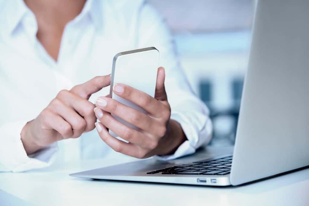 A person on a cell phone next to a laptop computer